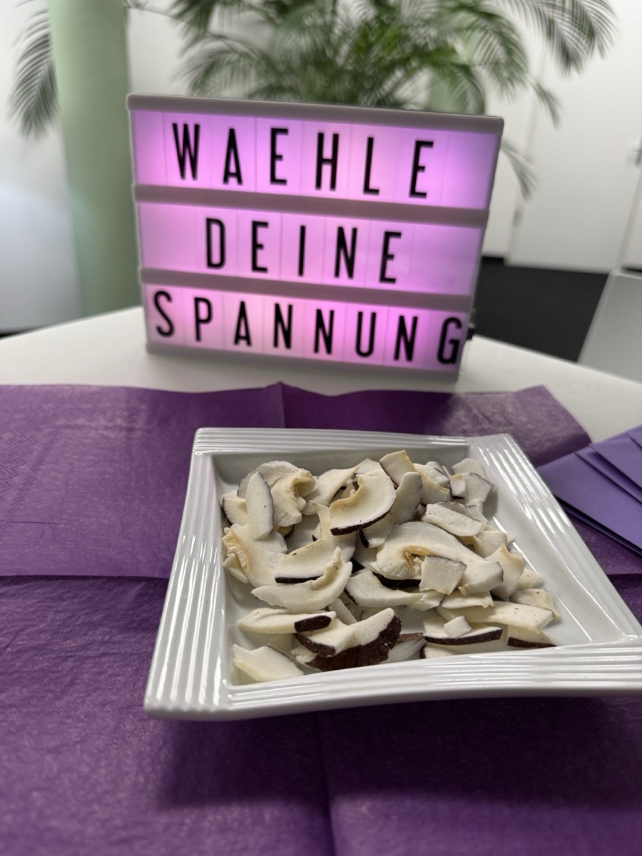 Detailaufnahme vom tiefwelt. Leadership Dinner: Lightbox-Schild „Wähle deine Spannung“ und eine Schale mit Kokoschips auf lila Tischdekoration